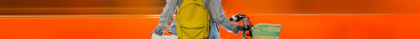 Teenager girl in jeans with yellow backpack and bike standing on metro station, waiting for train, smiling, laughing. Orange train passing by behind the girl. Futuristic subway station. Finland, Espoo